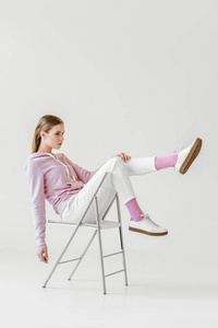 时尚的年轻女子在粉红色的帽衫坐在椅子上的白色和看远