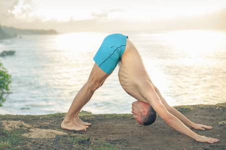 英俊的男人做瑜伽在悬崖与蔚蓝的大海背景