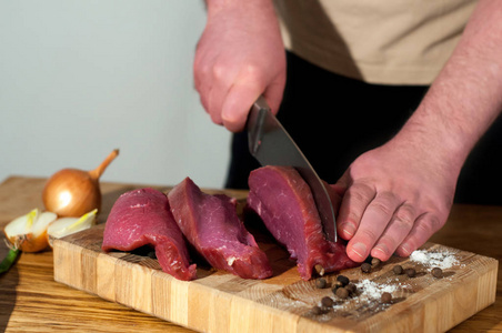 男人煮牛肉肉。男厨师准备猪肉做饭。原料洋葱肉盐椒在木桌上烹调牛肉肉