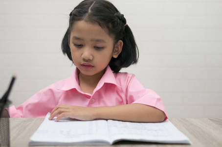 那个小女孩正在做作业。孩子们在木桌上看笔记本。选择 焦点浅景深 字段