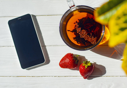 特写图像的玻璃杯茶, 红色草莓, 智能手机上的轻木背景