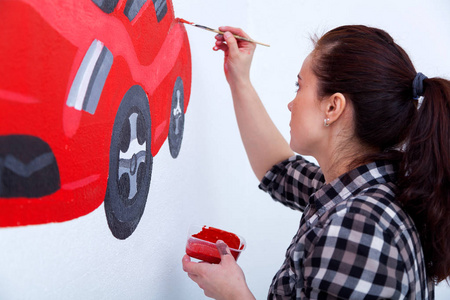 年轻的妇女画家和母亲男孩画一个孩子在白色墙壁一辆美丽的红色汽车在一个轻的孩子的房间里