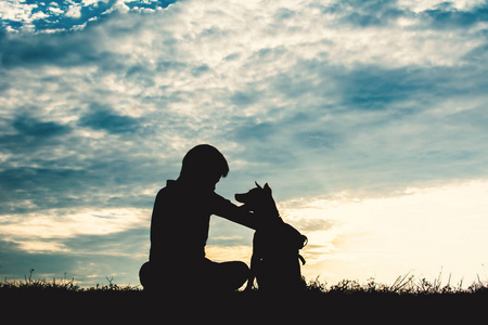 剪影可爱的男孩和狗玩在天空日落在假日