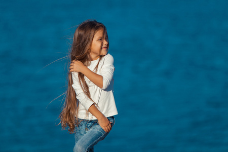 可爱快乐微笑的小女孩在海滩度假。牛仔裤