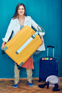 微笑的妇女拿着沉重的手提箱在蓝色背景, 旅行概念
