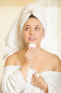 担心美丽的年轻女子，用白毛巾捂着头部清洗她的下巴，用一块小小的纸在浴室里