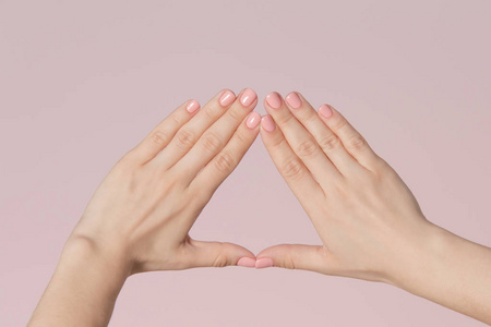 妇女手制作三角形框架孤立的粉红色背景。有粉红色指甲的女人手指。美容背景