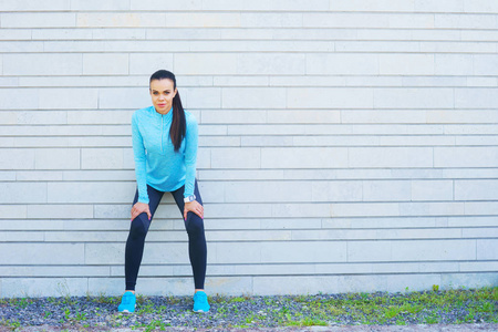 年轻, 健美和运动的妇女站在水泥墙前。健身运动城市慢跑和健康生活方式概念