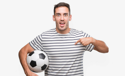 英俊的年轻人拿着足球带着惊讶的脸指着自己