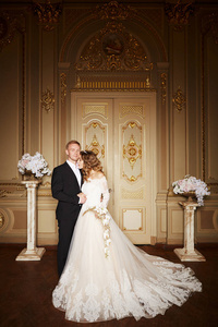 豪华婚礼情侣恋爱。美丽的新娘在白色礼服与新娘花束和英俊的新郎穿着黑色西装站在巴洛克内部和拥抱对方