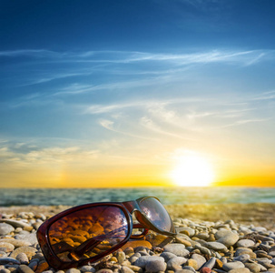 特写太阳镜躺在海上海岸上的戏剧性日落背景