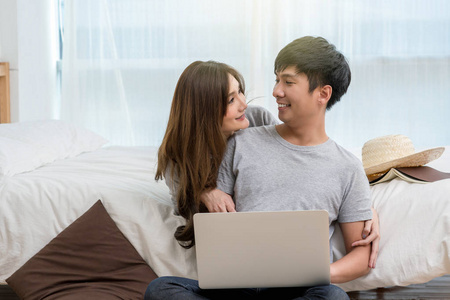 特写愉快的亚洲恋人或夫妇交谈和微笑当使用技术笔记本电脑在床上的现代家, 年轻女性指向男友, 情人和生活方式概念的鼻子