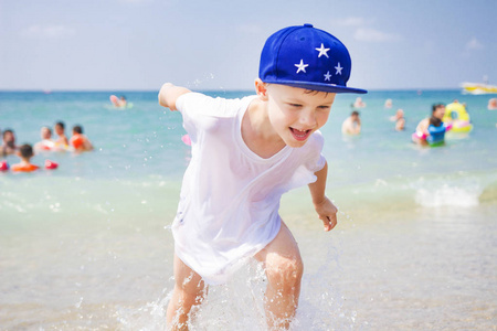 快乐男孩沐浴。小男孩沿着海边奔跑, 在晴朗的夏日里, 在海上游泳的人的背景下。在海边的暑假里, 孩子在海滩上玩得很开心。海上好日