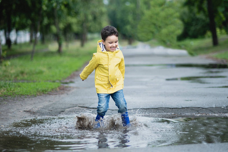 小男孩在雨衣和橡胶靴在水坑里玩