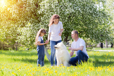 丈夫妻子和小女儿穿着白色的衣服和牛仔裤, 连同一只白狗, 在花园里休息。