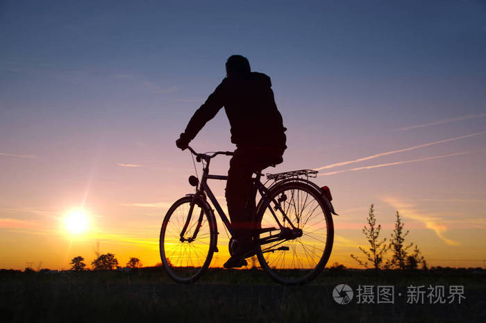 车手剪影在复古自行车与日落天空背景.健康的娱乐和活动