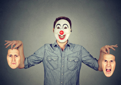 人在快乐的小丑面具拿着两张脸，表达愤怒和悲伤