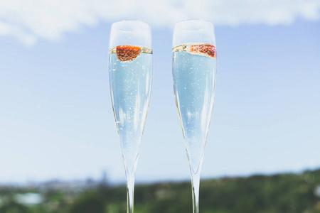 两个香槟眼镜与草莓在阳光明媚的露台室外庭院俯瞰干净的蓝天在夏天的城市外。特写视图