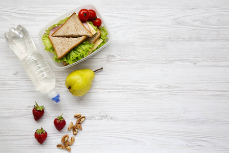 健康学校午餐盒配有新鲜有机蔬菜三明治核桃瓶装水和水果白色木质背景, 平躺。从上面。顶部视图。复制空间