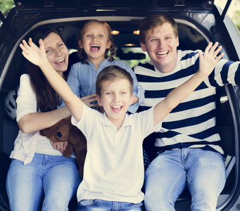 父母和孩子们坐在汽车后备箱里, 一家人正在去旅行。