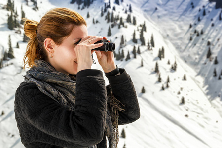 美丽的女孩看通过望远镜在雪山背景下