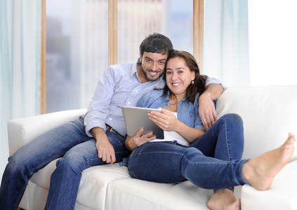 年轻的拉丁快乐夫妇在家里的沙发上享受使用数字平板电脑
