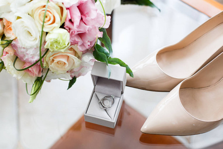 结婚戒指与钻石, 鞋子和婚礼花束在玻璃桌上