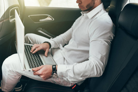 自信的年轻商人在他的笔记本电脑上工作, 而坐在车上