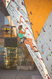登山者用人工的浮雕训练。一个女人爬上一条爬在爬墙上的登山路线。训练在大厅里