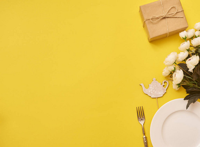 圆白色空盘子与叉子, 礼物盒和白色花在黄色背景。顶部视图