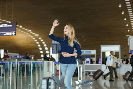 学生站在机场大厅的智能手机, 手提箱和举手