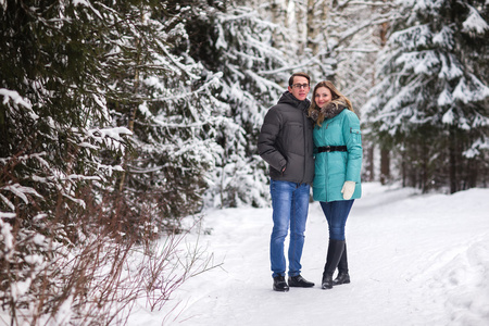 年轻美丽的夫妇在冬季森林散步