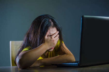 年轻的悲伤和惊恐的妇女的戏剧性的肖像覆盖面用手强调和担心看在黑暗背景下的笔记本电脑网络欺凌和互联网问题