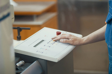 工人的手按下印刷机控制面板上的按钮