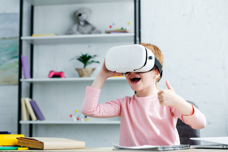 可爱的快乐学童使用虚拟现实耳机和显示拇指向上