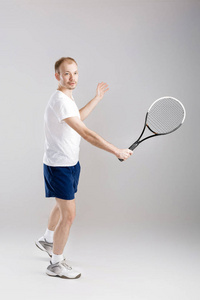 年轻的网球运动员打网球在灰色的背景上