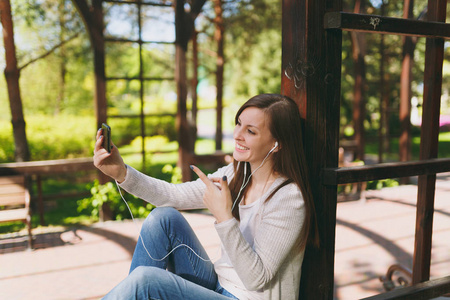 穿浅色休闲服的漂亮女人肖像。微笑的女性坐在城市公园的户外街道上的春天自然, 做自拍拍摄的手机或视频通话。生活方式概念