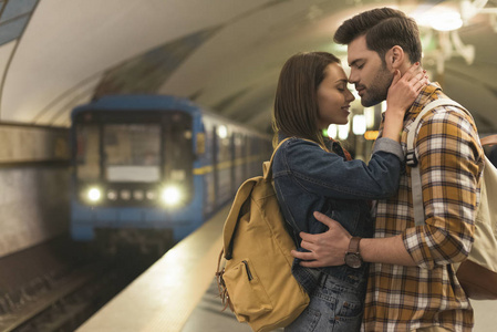 在地铁站互相拥抱的时尚情侣的侧面视图