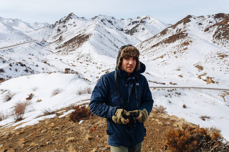 一个愉快的旅行者与照相机站立在被雪覆盖的山之中哈萨克斯坦