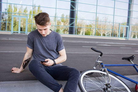 年轻的时髦发短信的手机，在城市街道上的固定的齿轮自行车。大镜子 windows 背景