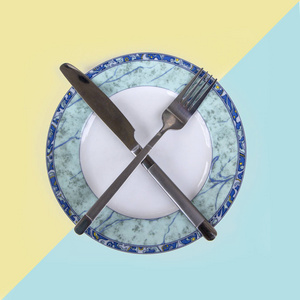 交叉叉和刀躺在一个空白色与蓝板, 餐具为晚餐, 孤立在温和的黄色蓝色背景, 顶部视图