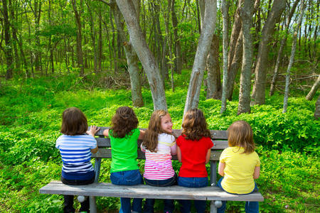 坐在森林公园长凳上的小妹妹和小朋友