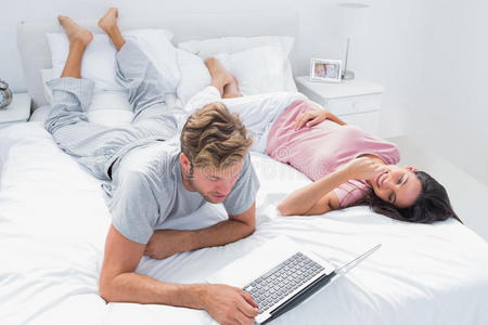 躺在床上的妻子旁边用笔记本电脑的男人