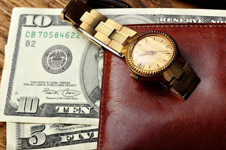优雅的金色手表和棕色钱包用木制的桌子上的钱