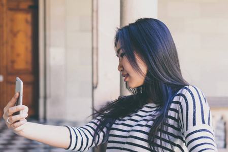 在参观城市博物馆的时候, 一个迷人的亚洲女性带着深色长发穿条纹长袖 t恤衫的侧面照片, 自拍用手机相机拍摄