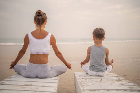 一位母亲和儿子正在做瑜伽练习在热带海洋的海滨