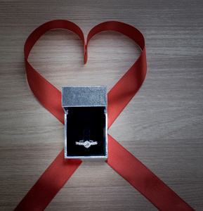 木制表面上的结婚戒指和红色心丝带