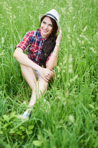 美丽的女人在夏天的衣服和帽子坐在草地上草
