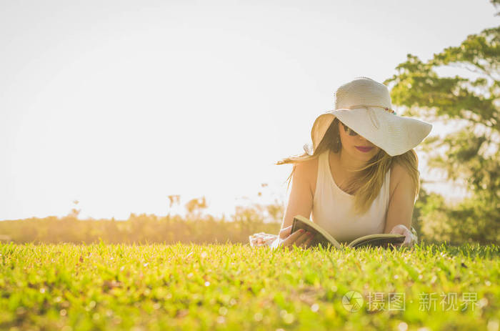 漂亮的女人看书躺在草坪上, 从上面看到夏天的帽子