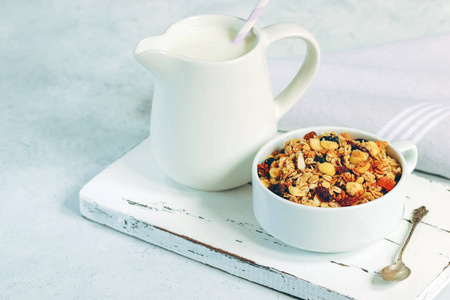 杯麦片与热带水果和白色牛奶壶在木板上。纯色调健康饮食理念